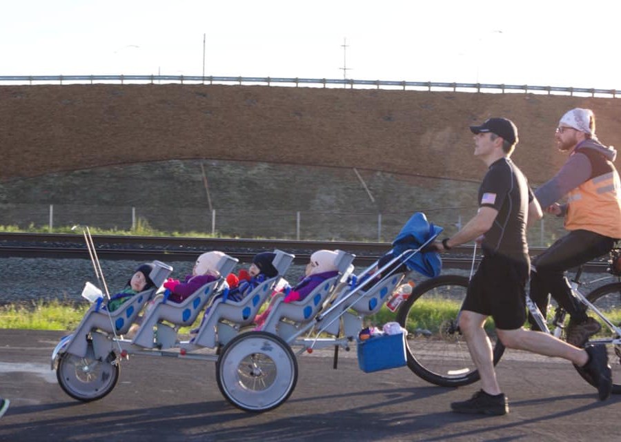 Chad Kempel pushing his quintuplets in a five-seat stroller during the 2019 Modesto Marathon while his brother Steven rides a bike alongside