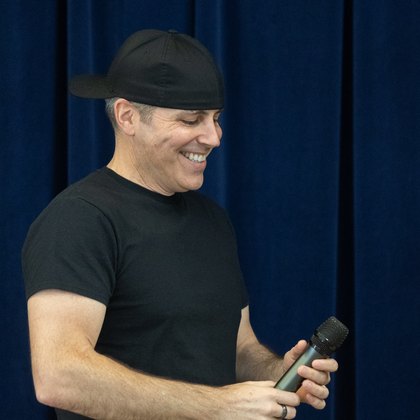 Chad Kempel, graduation and commencement speaker, smiling on stage with a microphone