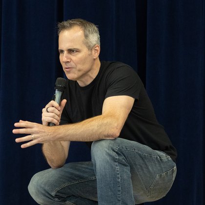 Chad Kempel, mental health assembly speaker, crouching on stage as he speaks