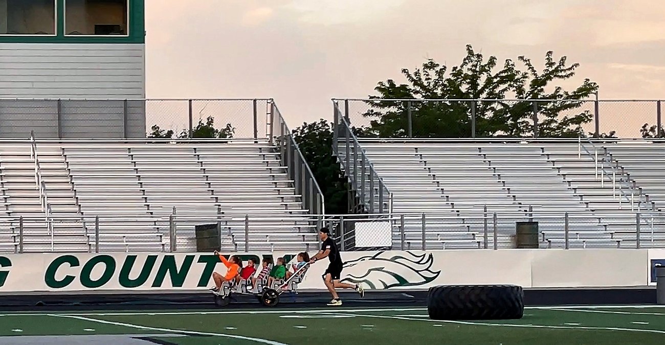 Chad Kempel pushing a five-seat stroller with five children past the Mustang Country wall and empty bleachers at the Eagle High School track in Eagle, Idaho, during his 1K Guinness World Records run