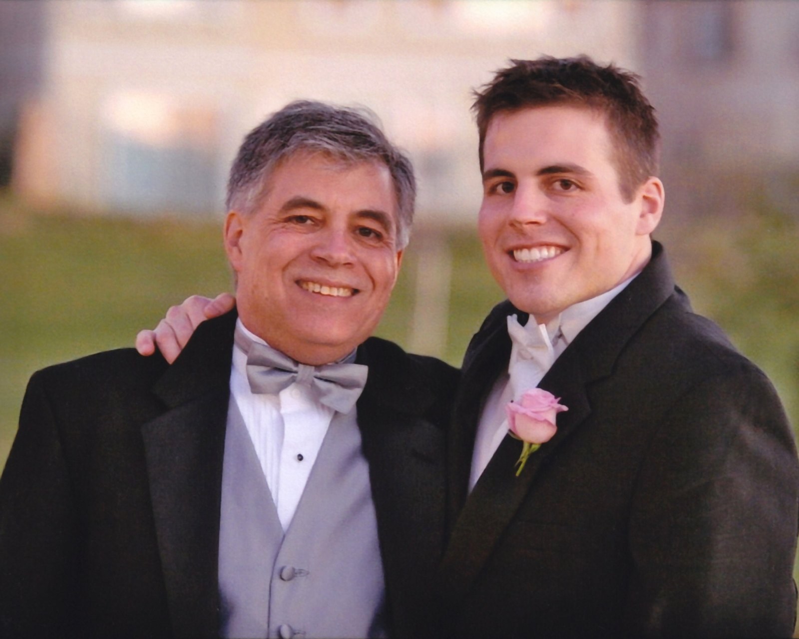 Paul Kempel in a gray vest and bow tie with his arm around his son Chad Kempel, both smiling, at Chad's wedding