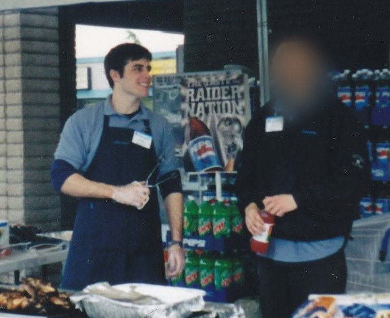 Chad Kempel in an apron grilling outside the grocery store where he worked, next to his friend, whose face is blurred