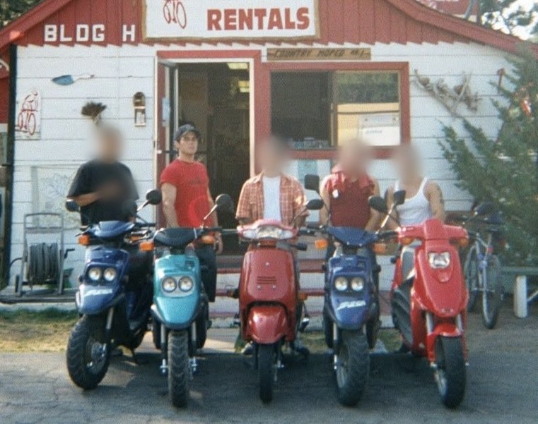 Chad Kempel in a red shirt with four friends, faces blurred, lined up with rental scooters outside a rental shop in Lake Tahoe