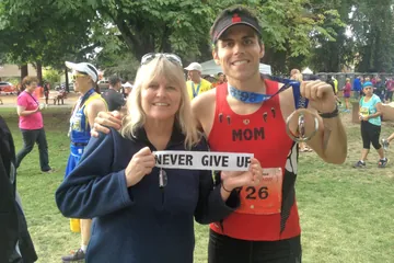 Chad Kempel holding his finisher medal after the 2013 Santa Rosa Marathon, next to a woman holding a Never Give Up sign