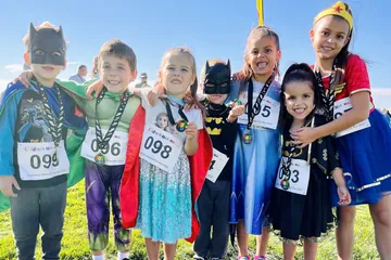 All seven Kempel kids in superhero costumes with their medals at the 2022 Superhero Obstacle Fun Run