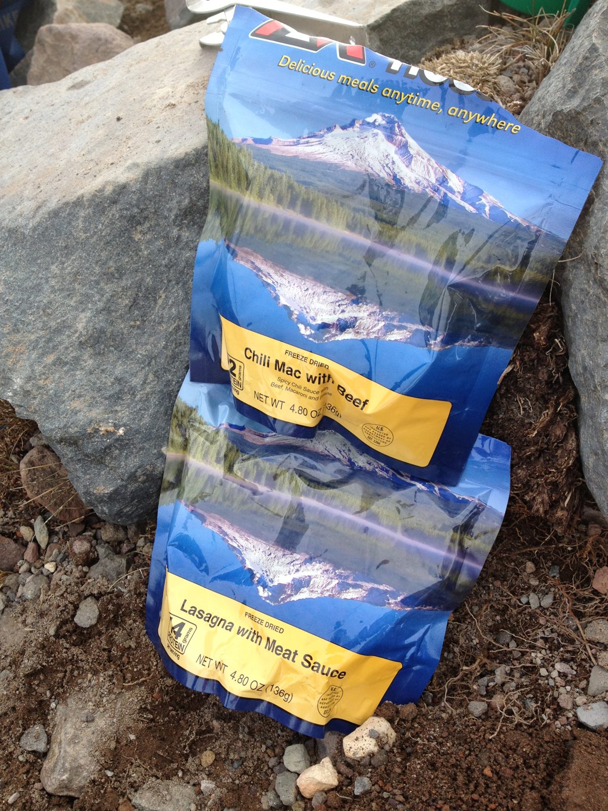 Two empty freeze-dried meal pouches, chili mac and lasagna, leaning against a rock at camp on Mt. Shasta