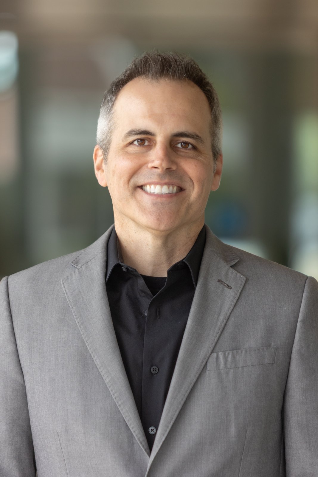 Chad Kempel, smiling studio portrait in grey blazer
