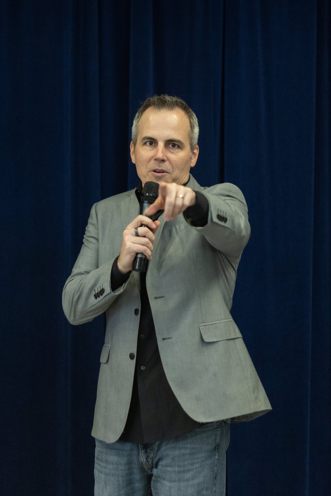 Chad Kempel pointing toward the audience while speaking with a microphone